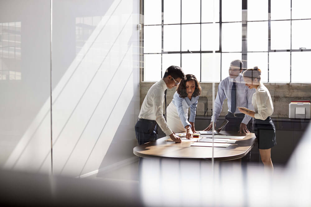 four coworkers collaborating at a conference room table in front of a window 