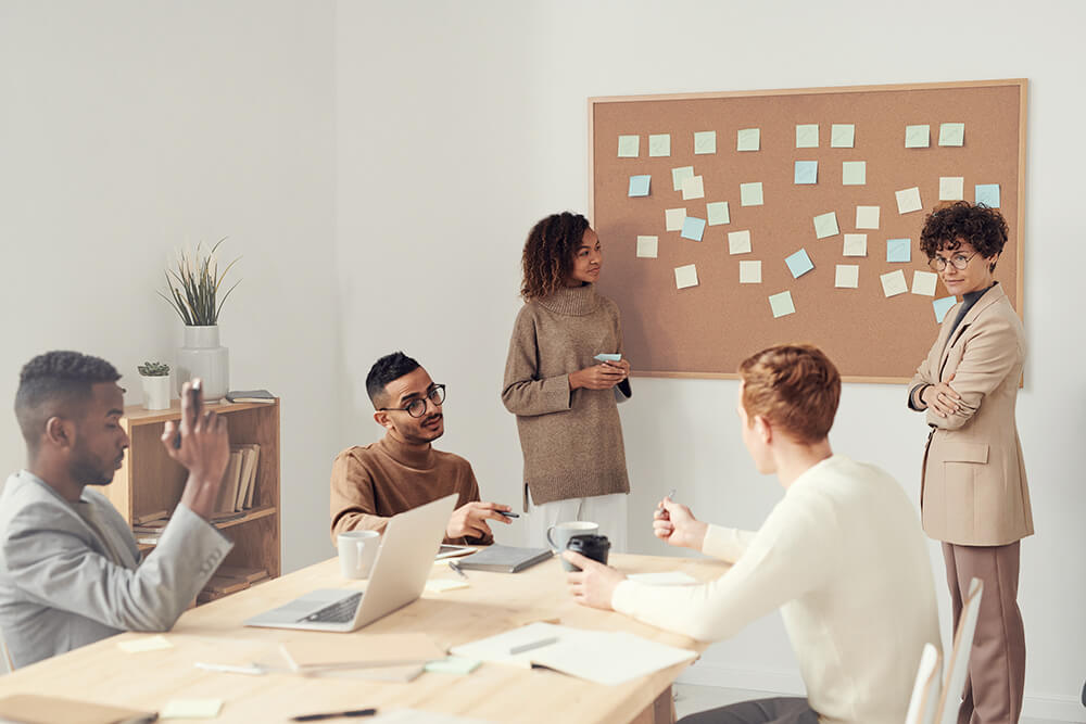 group of coworkers in a meeting with post-its on a corkboard 