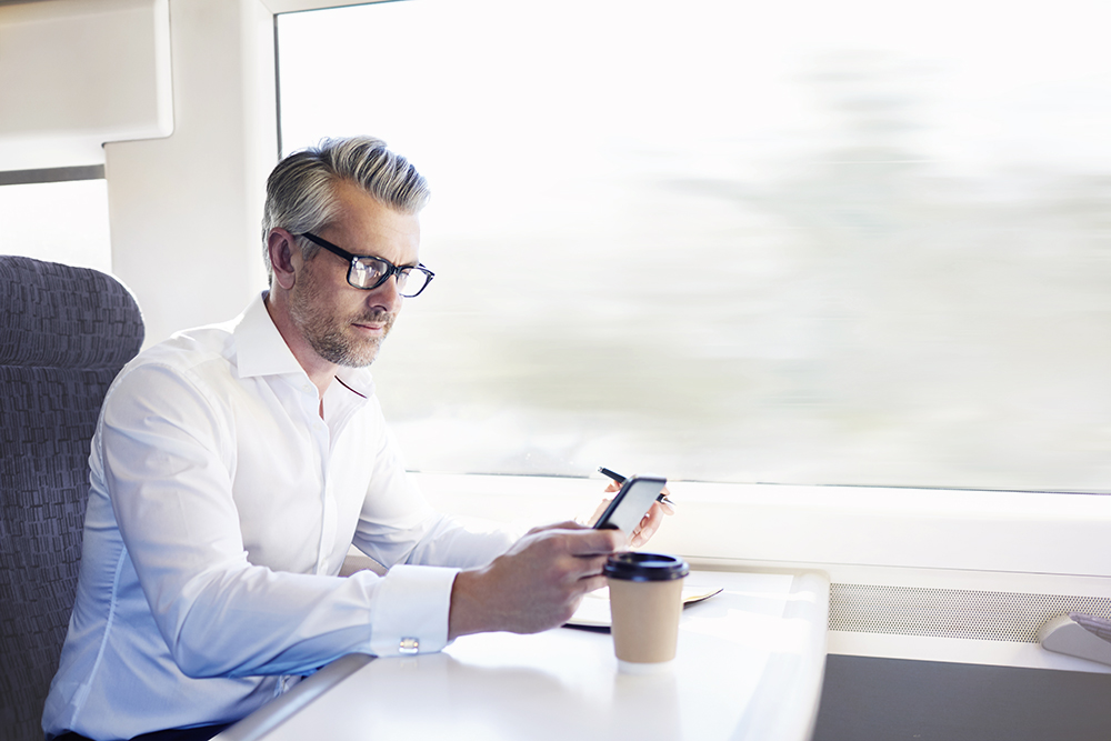 man on train with a to-go coffee, looking at phone