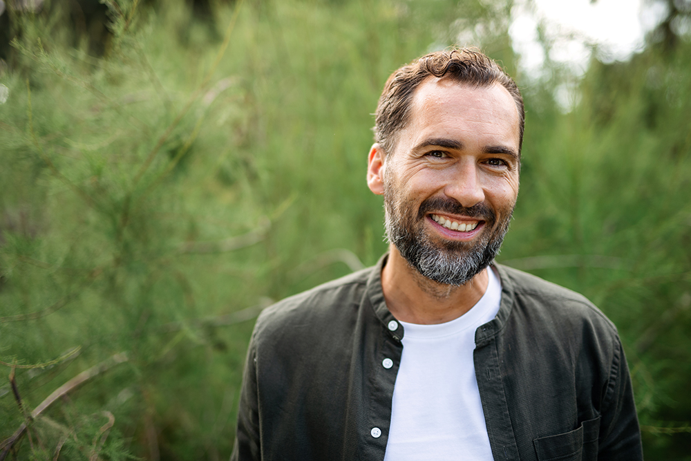 close-up of bearded white man in front of greenery