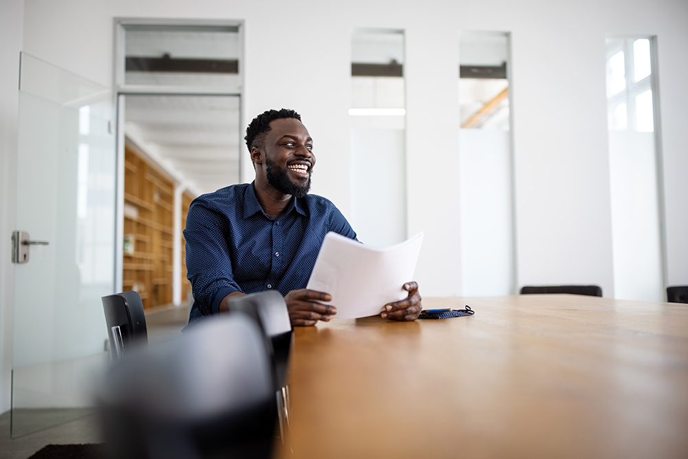 black man smiling, sitting alone at a conference table 