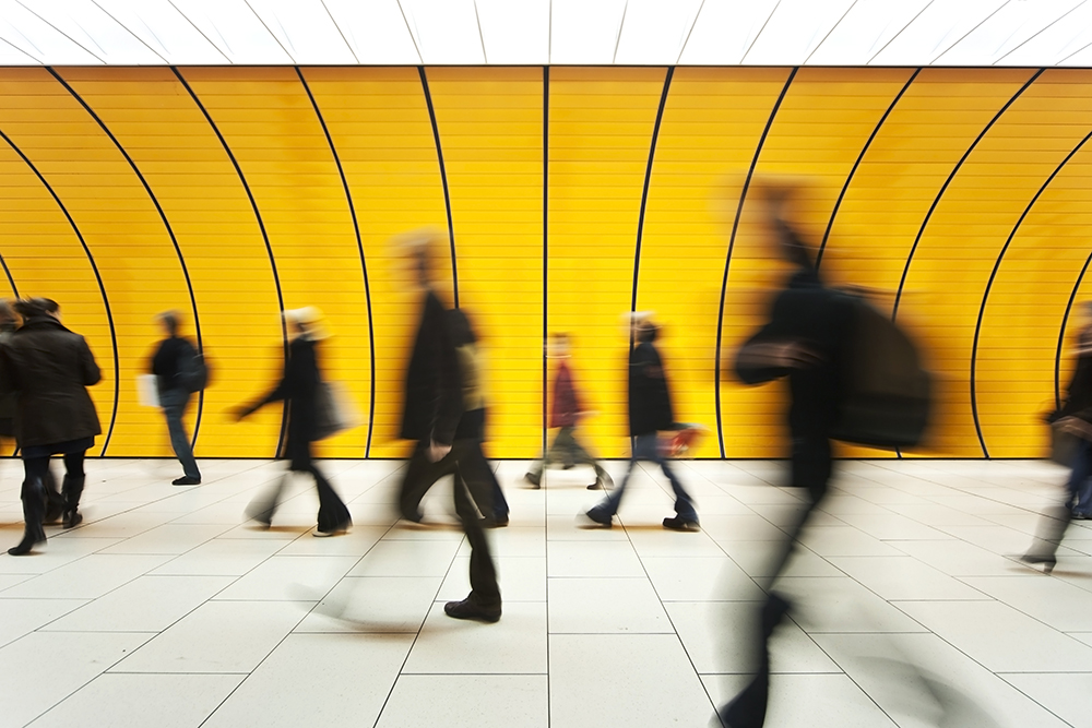 blurry walking commuters against an orange yellow wall