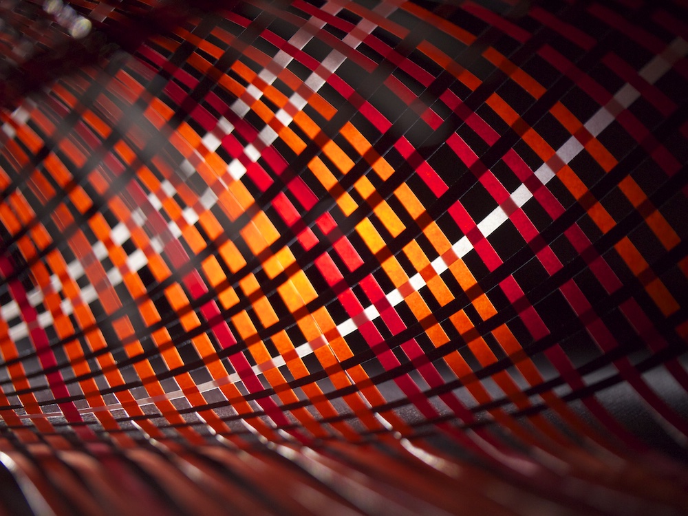 Close-up of a curved surface covered with a geometric pattern of interwoven red, orange, and black rectangles, creating an abstract, visually dynamic effect.