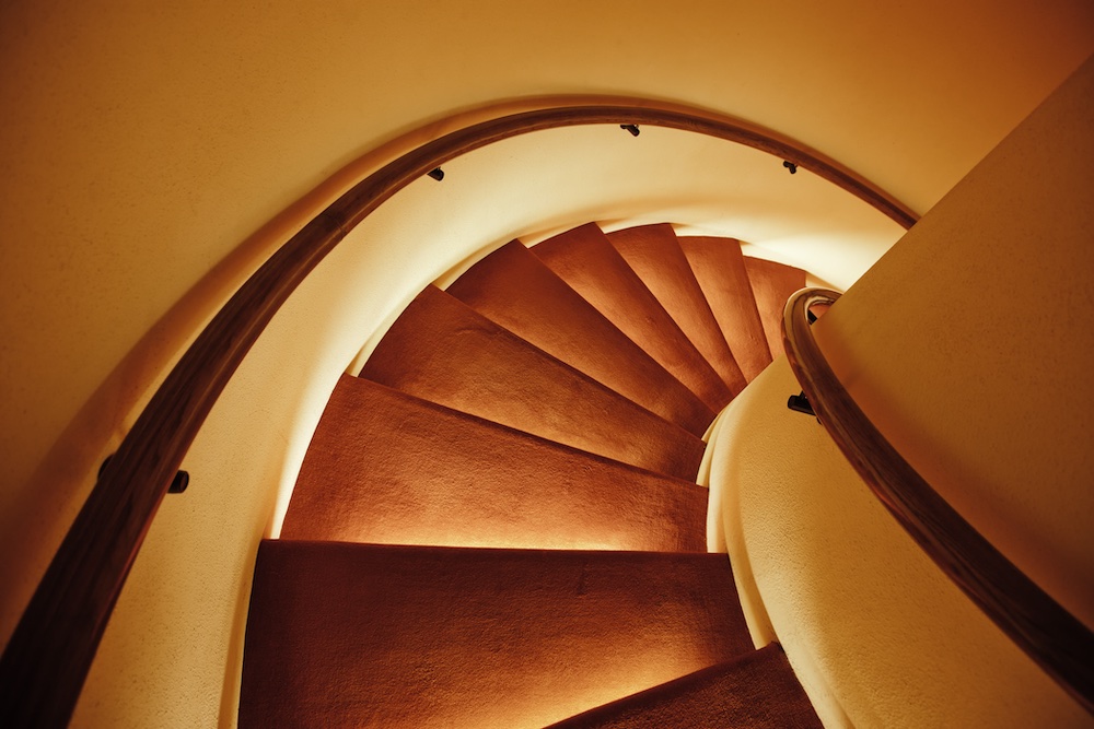 A spiral staircase with warm, yellow lighting underneath the steps and wooden handrails, creating a cozy and elegant atmosphere. The photo is taken from above, highlighting the curved design.
