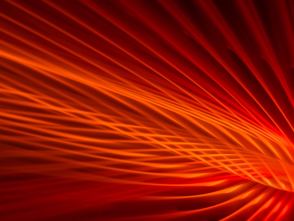Abstract image of overlapping, bright orange and red lines creating a dynamic, flowing pattern against a dark background, resembling light trails or waves.