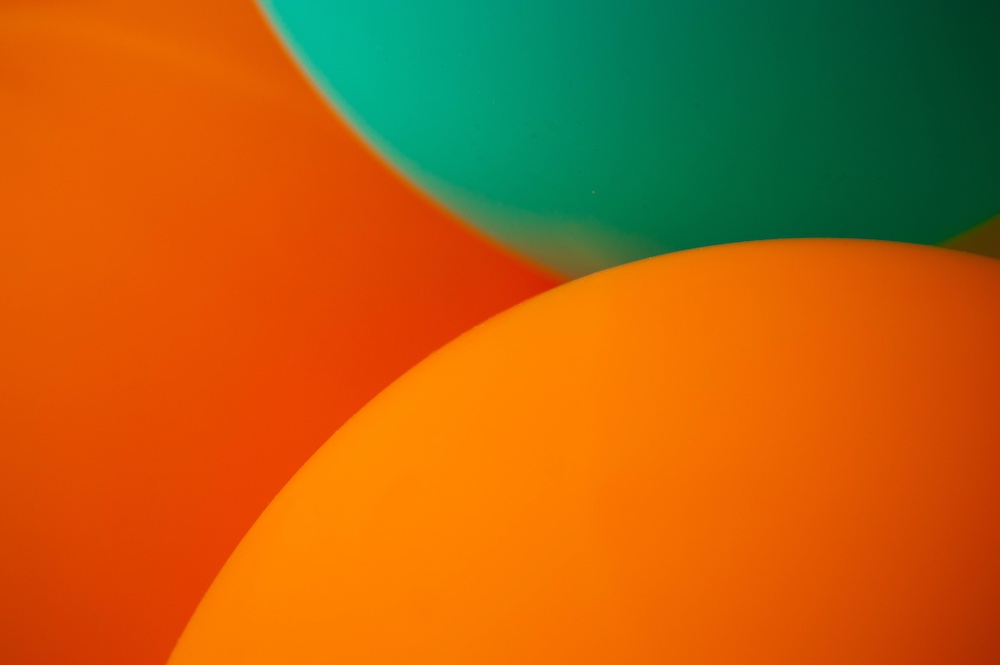 Close-up of three balloons, two orange and one teal, overlapping each other to create a colorful and festive abstract pattern.
