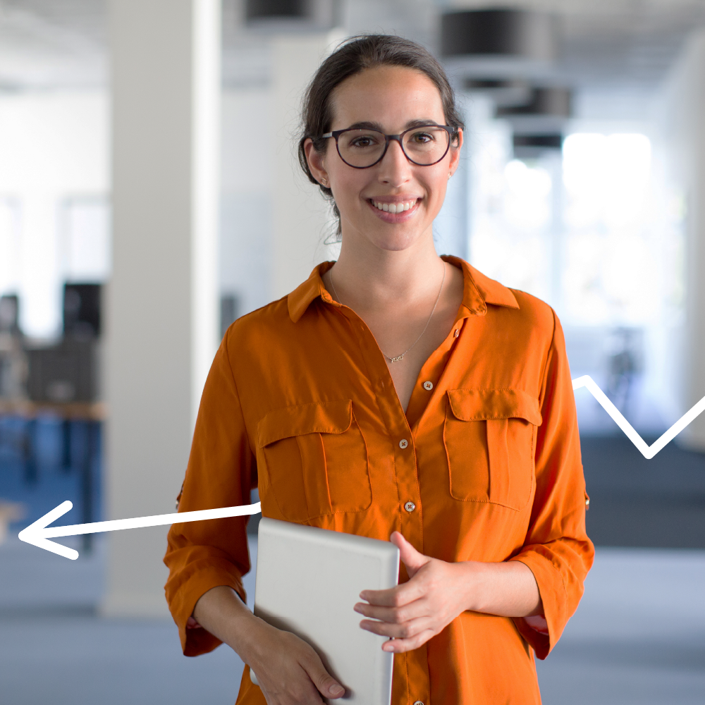 A smiling woman in an orange shirt and glasses stands in an office, holding a closed laptop. White arrows are drawn on the image, pointing toward her. The background shows a modern, open workspace.