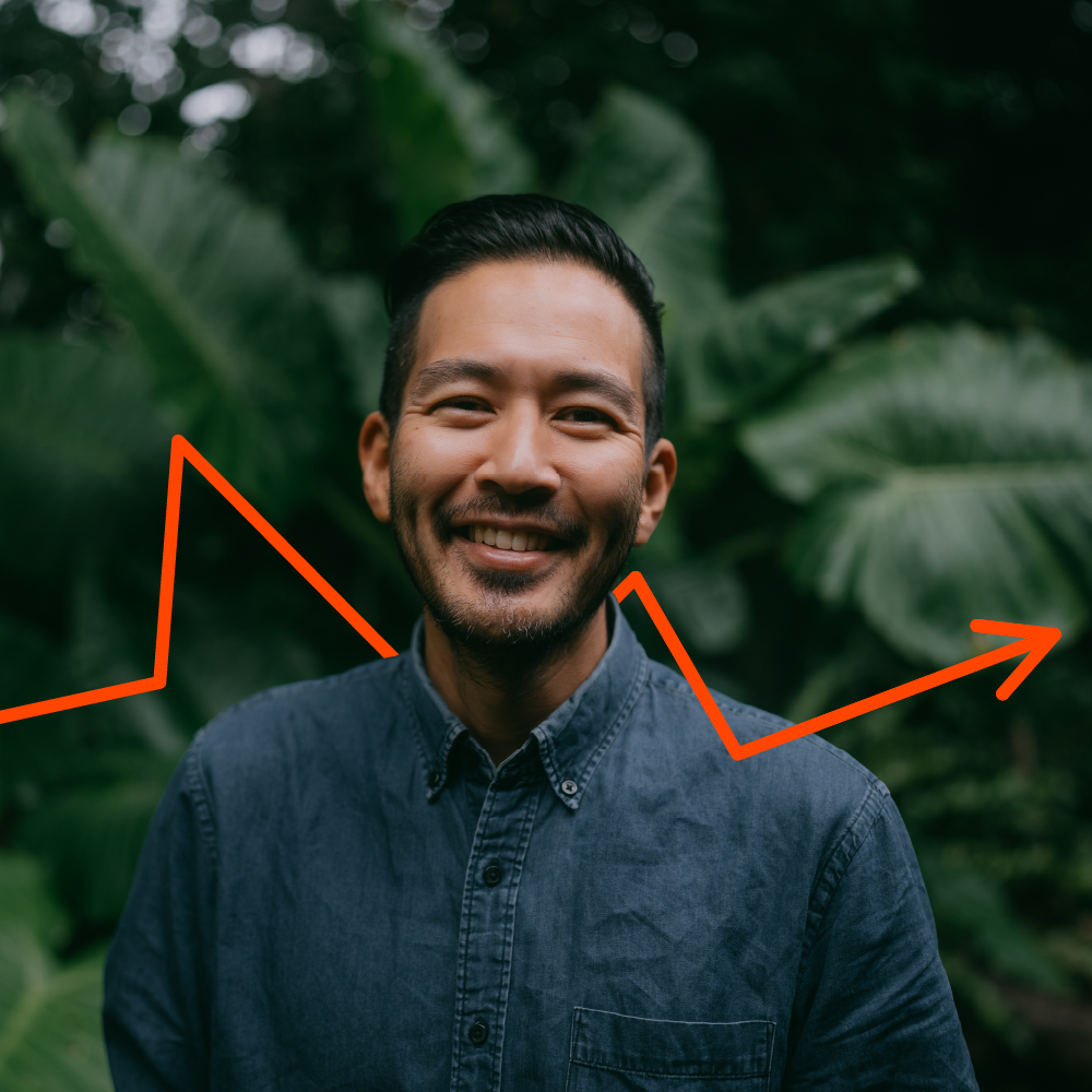 A smiling man in a denim shirt stands outdoors in front of lush green foliage, with an orange upward-trending arrow graphic superimposed diagonally behind him.